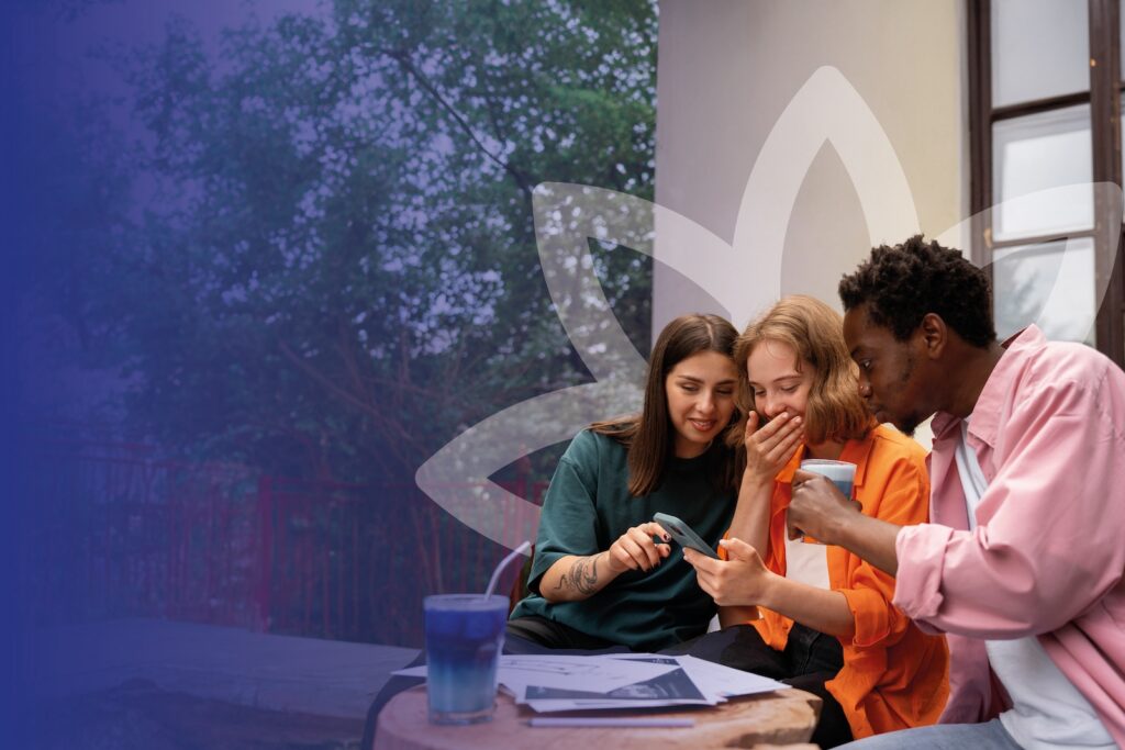 Three young adults sitting outside of a cafe reviewing the studying notes while having coffee together.