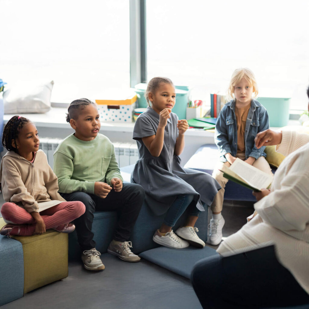 Four young children sat on cushions listing to their teacher read