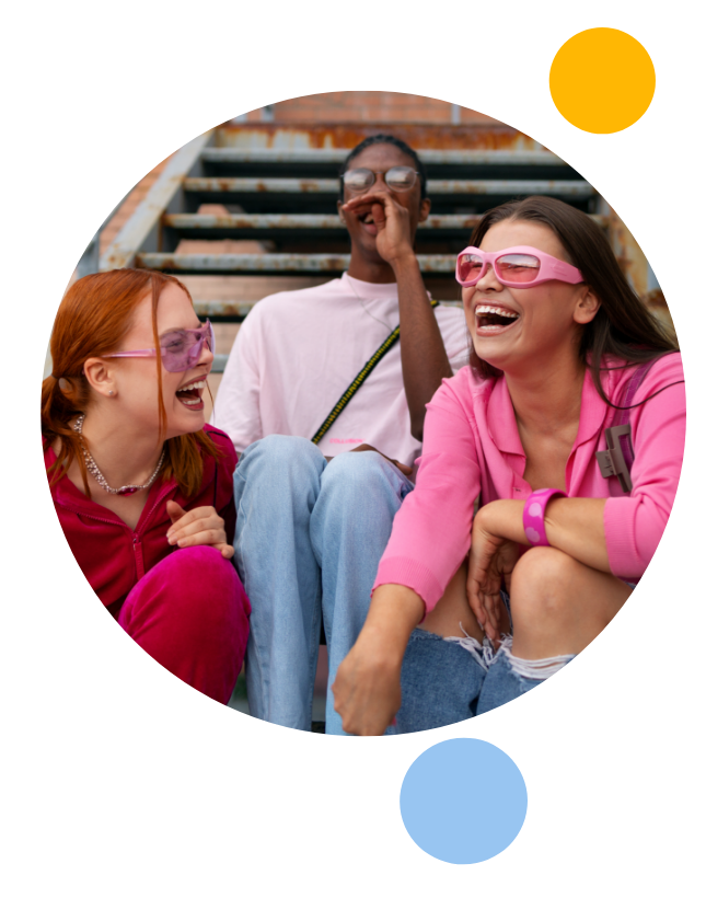 Three fashionable friends laughing on a staircase in a circle with blue, yellow and light blur circles surrounding them.