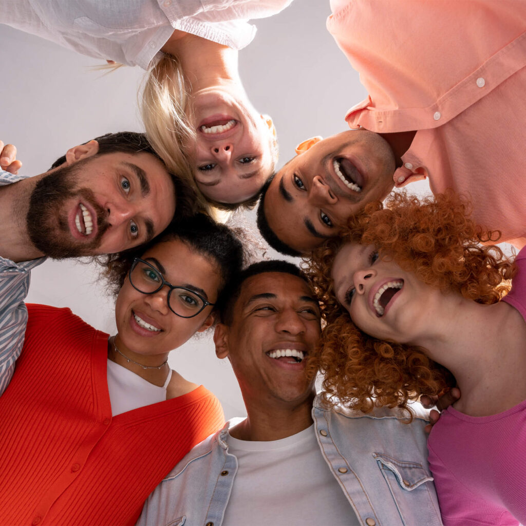 Six adults smiling and laughing as they stand in a circle staring at camera below them