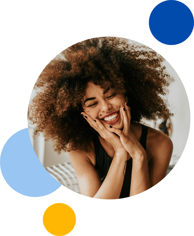 A young mixed-race woman smiling into her hands whilst she closes her eyes.