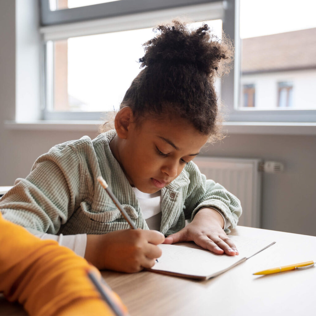 A young girl sat at her desk focused and writing in her small notebook