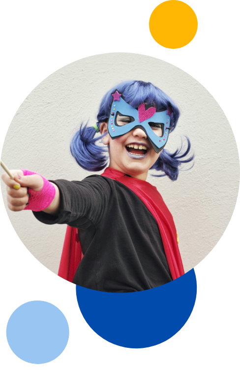 A young child wearing make up, purple wig, mask and cape. Striking a pose to the camera in a circle with blue, yellow and light blur circles surrounding them.