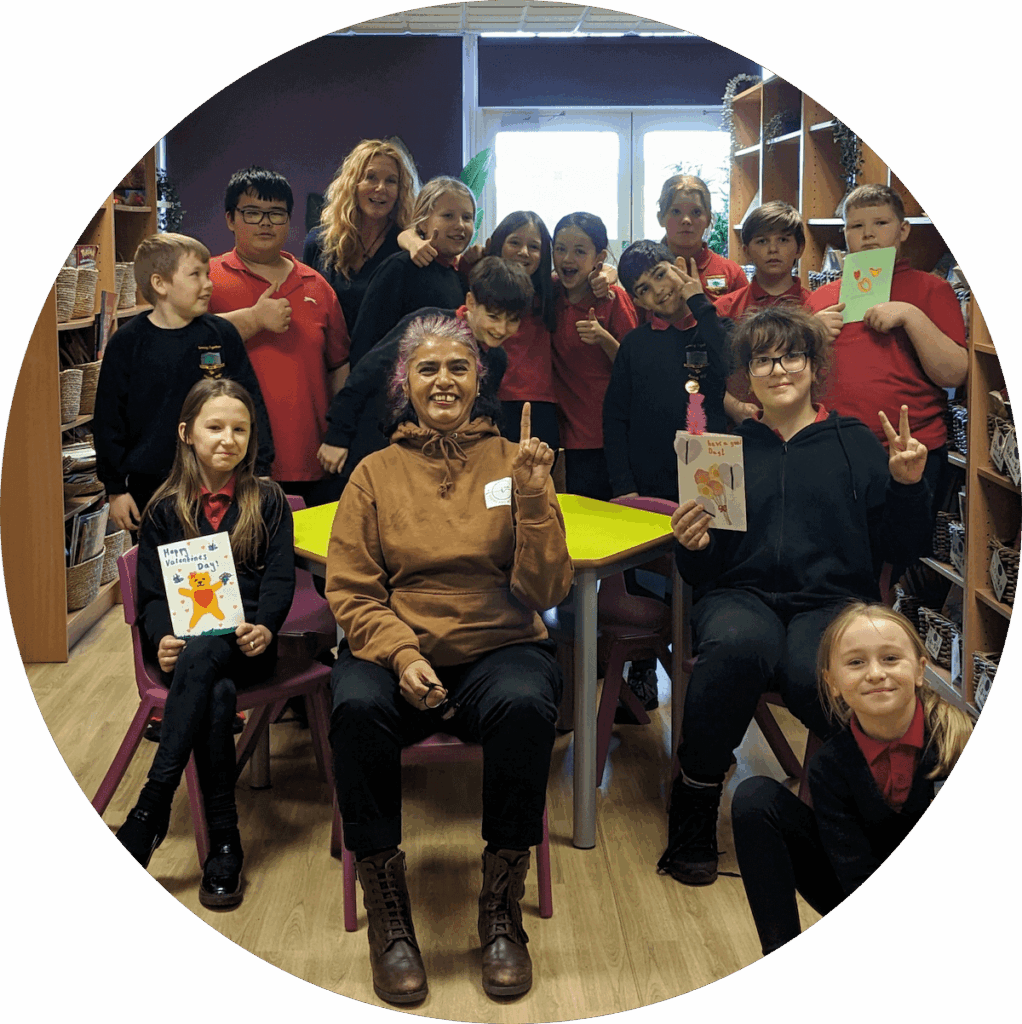 Shilpa and Geraldine surrounded by primary school students, as they smile and show off the work they made during their mindfulness session