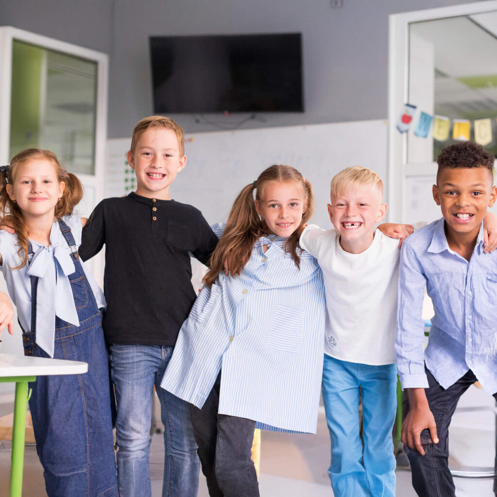 Five children with their arms wrapped around each others shoulders smiling at the camera